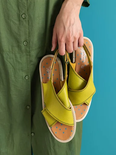 Hands holding a pair of yellow-green sandals from Gudrun Sjödén. 