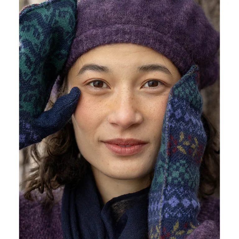 Close-up of a woman’s face and hands. Wearing knitted mittens from Gudrun Sjödén on her hands. 