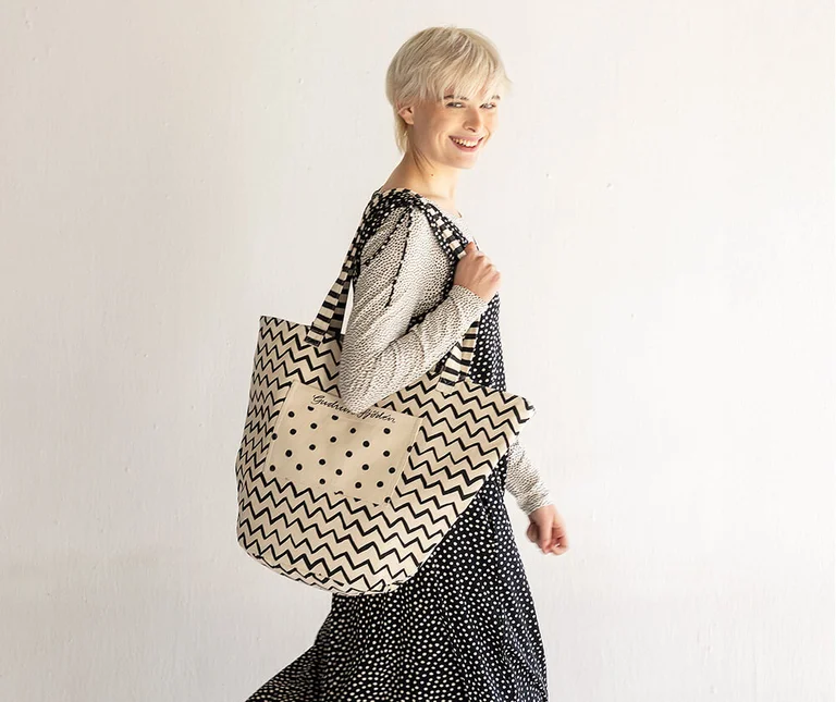 Ein Frau mit einer schwarz-weißen Stofftasche mit Zickzack- und Punktemuster von Gudrun Sjödén.