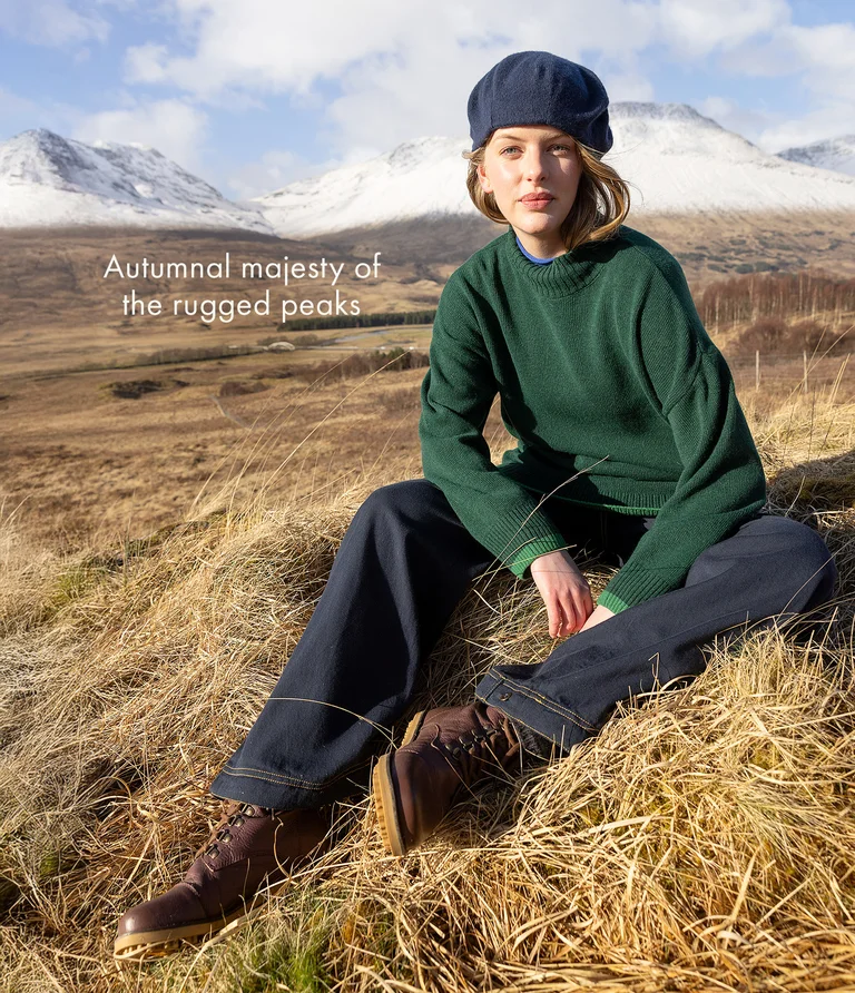 A woman sitting in a mountain setting wearing layers of clothing from Gudrun Sjödén. On her head, she is wearing a beret from Gudrun Sjödén.