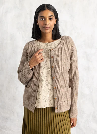 A woman wearing a beige knitted cardigan from Gudrun Sjödén.