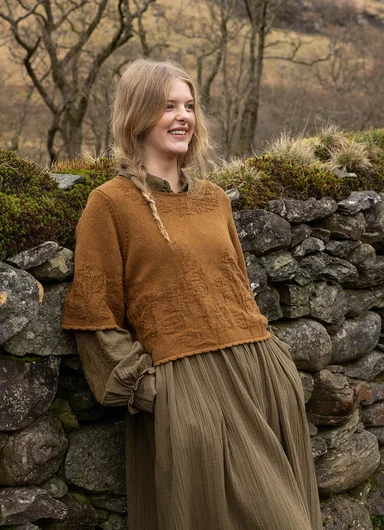 A woman leaning against a stone wall wearing clothes in earthy hues from Gudrun Sjödén.