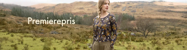 En kvinne i en langermet blomstret topp står i et naturlandskap med teksten "Premierepris".