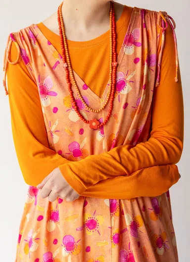 A close-up image of an upper body wearing a patterned orange dress and orange necklace from Gudrun Sjödén.
