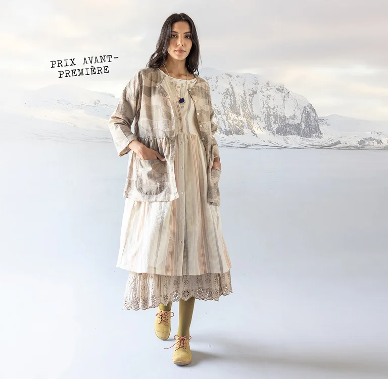 Une femme debout dans un paysage enneigé et portant des superpositions de vêtements blancs et beiges provenant de la collection de Noël 2025 de Gudrun Sjödén.