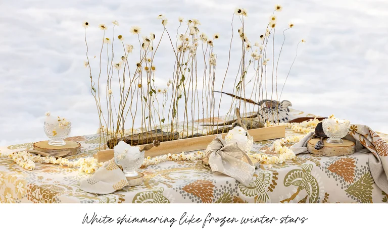 A table in the snow laid with home textiles from Gudrun Sjödén’s 2025 Christmas Home collection.