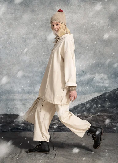 A woman mid-stride wearing white clothes and a knitted beanie from Gudrun Sjödén.