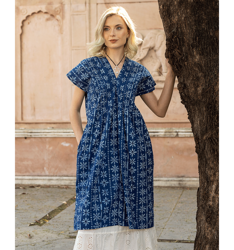 Eine Frau an einem Baum, in einem gemusterten blauen Kleid von Gudrun Sjödén.