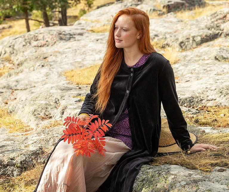En kvinne som sitter ned kledd i en svart velurkjole fra Gudrun Sjödén.