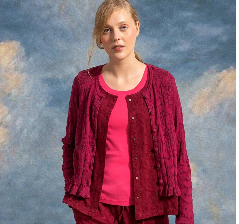 A woman holding one arm above her head, wearing a red knit dress over a light purple piece from Gudrun Sjödén.