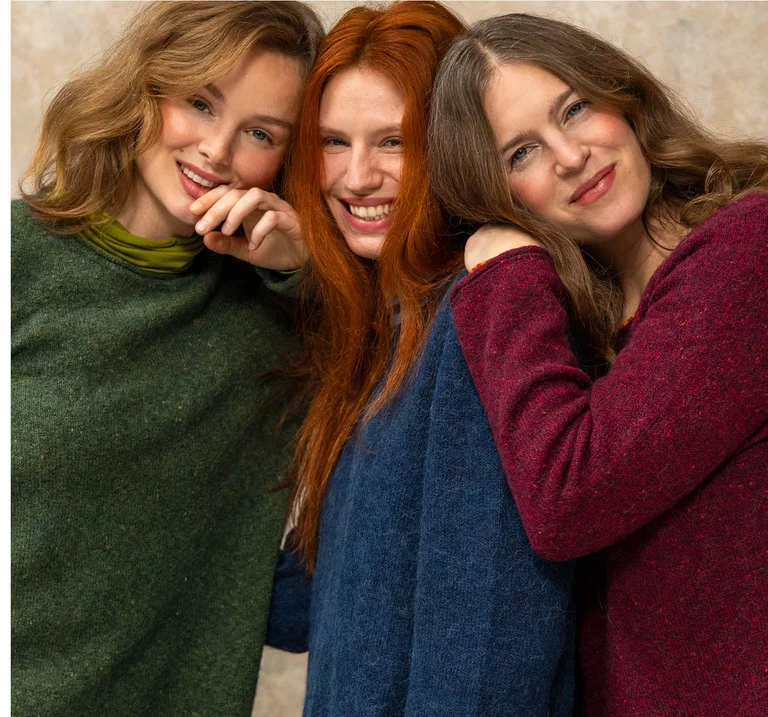 Trois femmes serrées l'une contre l’autre et portant des pulls de différentes couleurs signés Gudrun Sjödén.