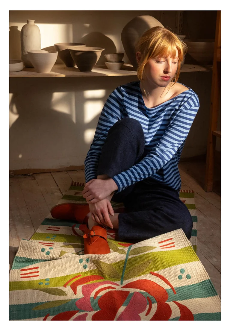 A woman in a striped top from Gudrun Sjödén, sitting on a rug from Gudrun Sjödén.