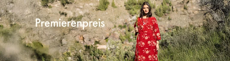 Eine Frau, die einen grünen Zweig vor ihrem Gesicht hält. Sie trägt ein rotes Wickelkleid von Gudrun Sjödén. 