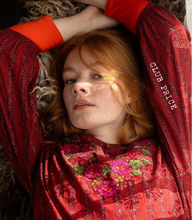 A woman lying down wearing a red, embroidered dress from Gudrun Sjödén’s 2025 Christmas collection.