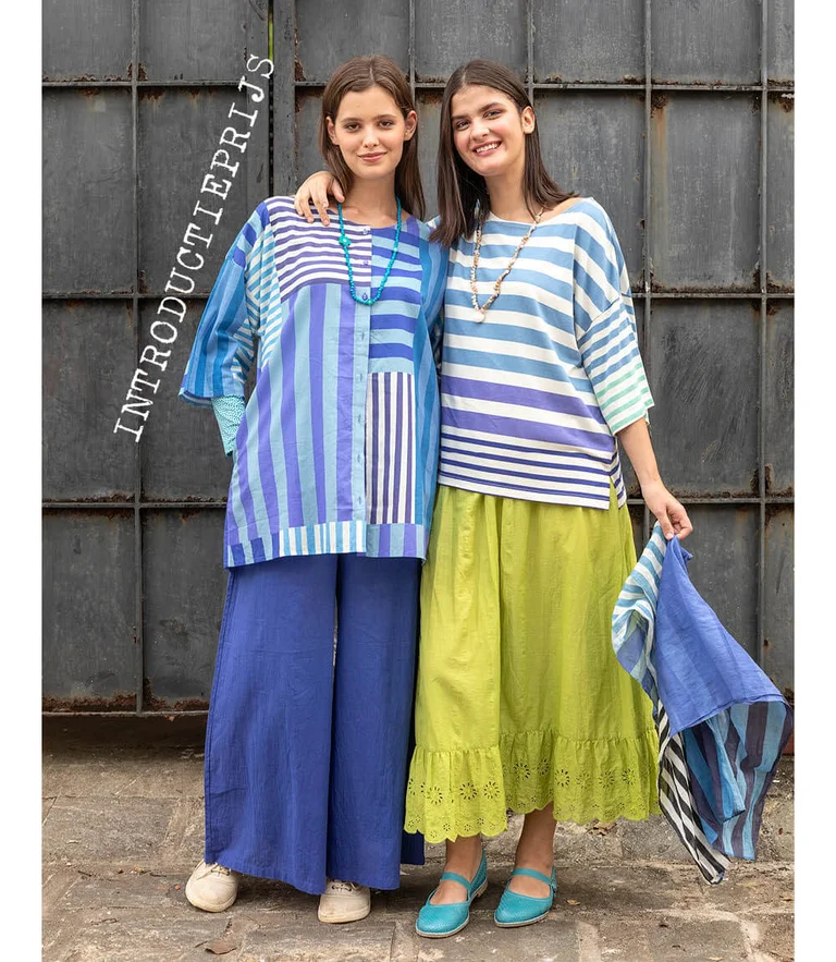 Twee vrouwen gekleed in gestreepte kledingstukken van Gudrun Sjödén. De ene vrouw heeft een bijpassende sjaal in haar hand.