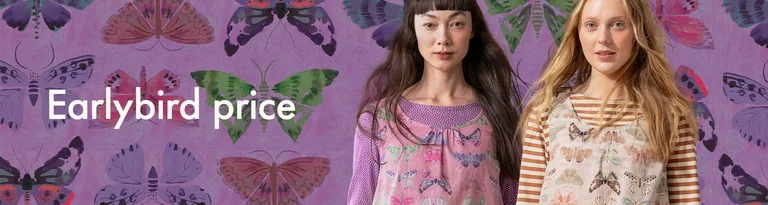 A woman standing by a wall wearing a ruffled blouse from Gudrun Sjödén. 