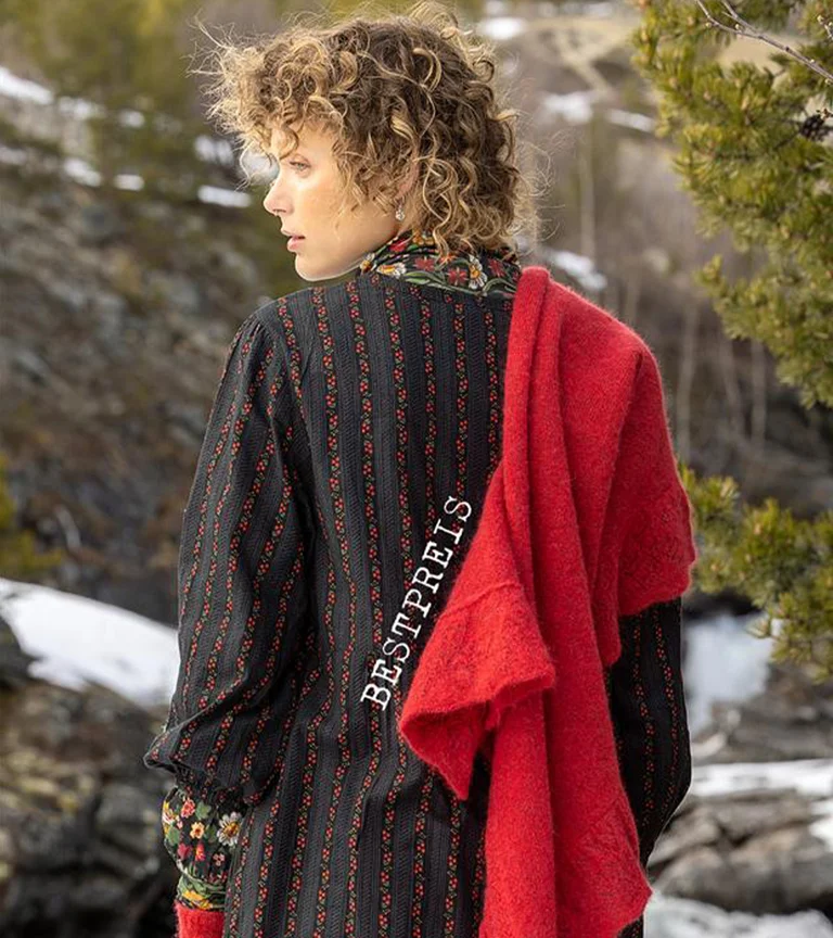 Eine liegende Frau in einem bestickten roten Kleid aus Gudrun Sjödéns Weihnachtskollektion 2025. 