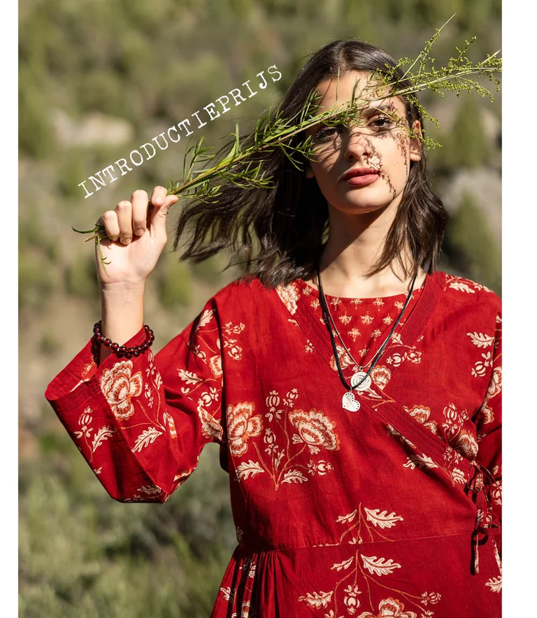 Een vrouw die een groene tak voor haar gezicht houdt en een rode overslagjurk van Gudrun Sjödén draagt. 