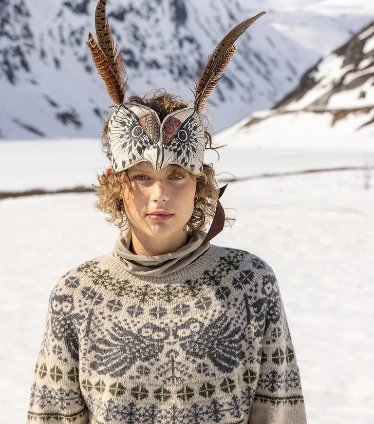 A close-up of a woman with an animal mask on her head in a snowy landscape wearing a knitted sweater from Gudrun Sjödén’s 2025 Christmas collection.