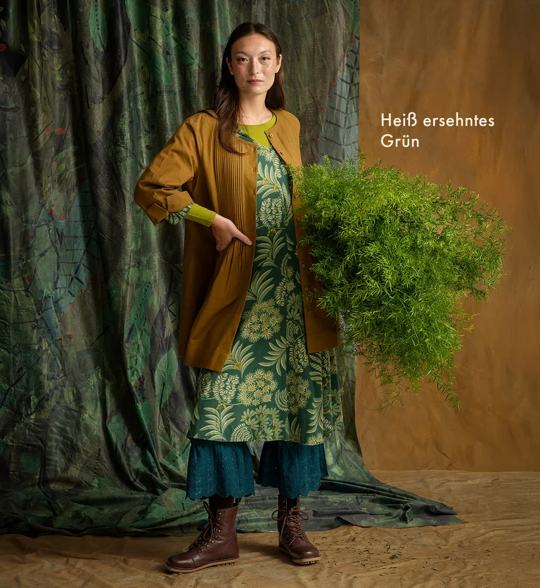 A woman holding a green plant, wearing layers of garments from Gudrun Sjödén.