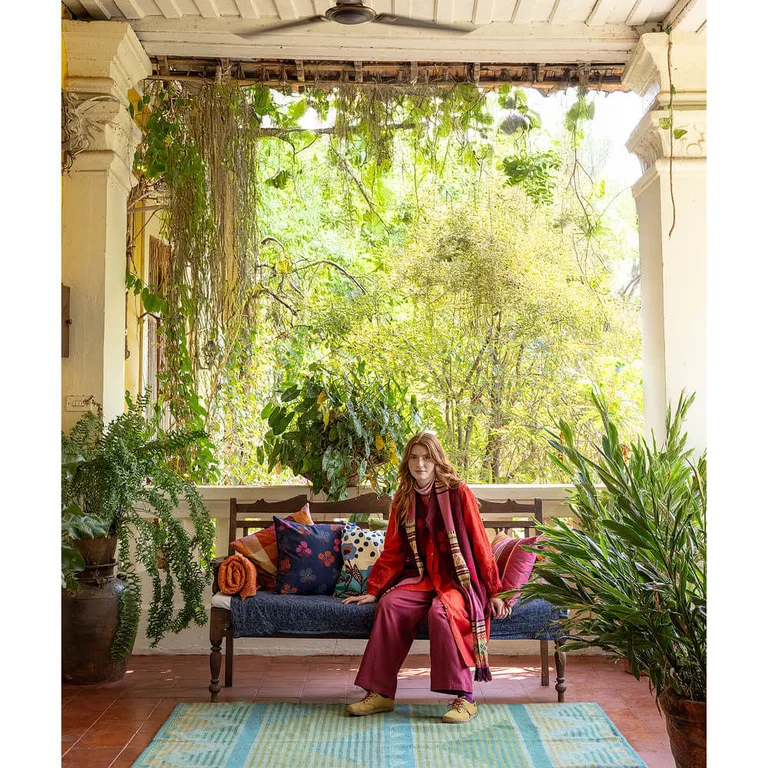 A woman wearing layered clothing from Gudrun Sjödén and seated among patterned cushions from Gudrun Sjödén. 