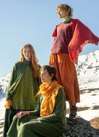 Three women wearing colourful red, pink and green winter clothes from Gudrun Sjödén’s Christmas collection, photographed in a mountain setting.