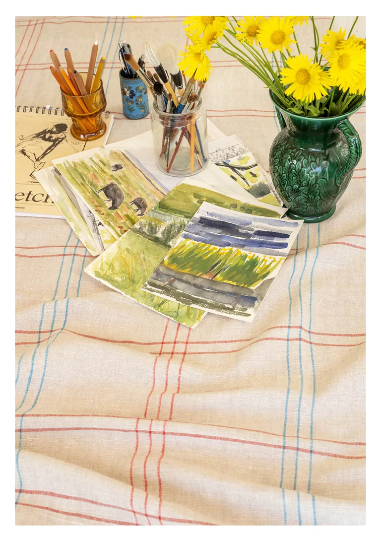 A checked tablecloth in a natural-colored linen blend from Gudrun Sjödén with watercolor paintings and brushes.