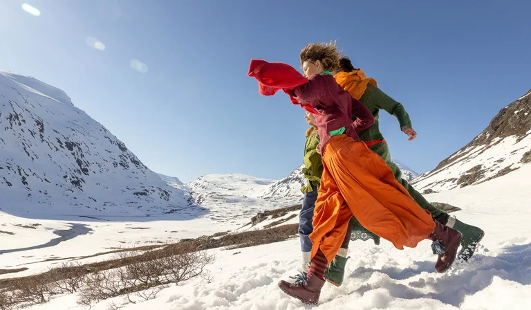 Zwei springende Frauen im Schnee, in farbenfroher Strickmode aus Gudrun Sjödéns Weihnachtskollektion 2025.