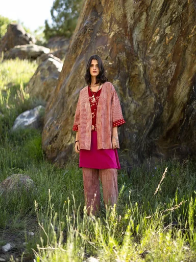 A woman standing in the countryside wearing layers of red clothes from Gudrun Sjödén. 