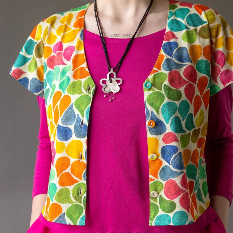 A close-up of the upper body of a woman wearing a pink top under a short-sleeve, patterned jersey top from Gudrun Sjödén. 