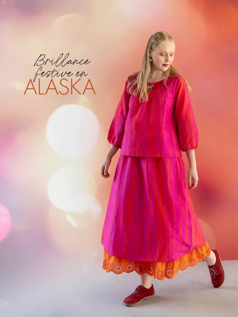 Une femme portant un top rose brillant et une jupe assortie provenant de la collection de Noël 2025 de Gudrun Sjödén. 