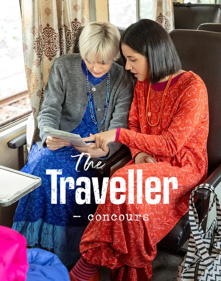 Two women on a train, leaning over a map, wearing layers of clothes from Gudrun Sjödén.