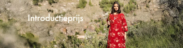 Een vrouw die een groene tak voor haar gezicht houdt en een rode overslagjurk van Gudrun Sjödén draagt.