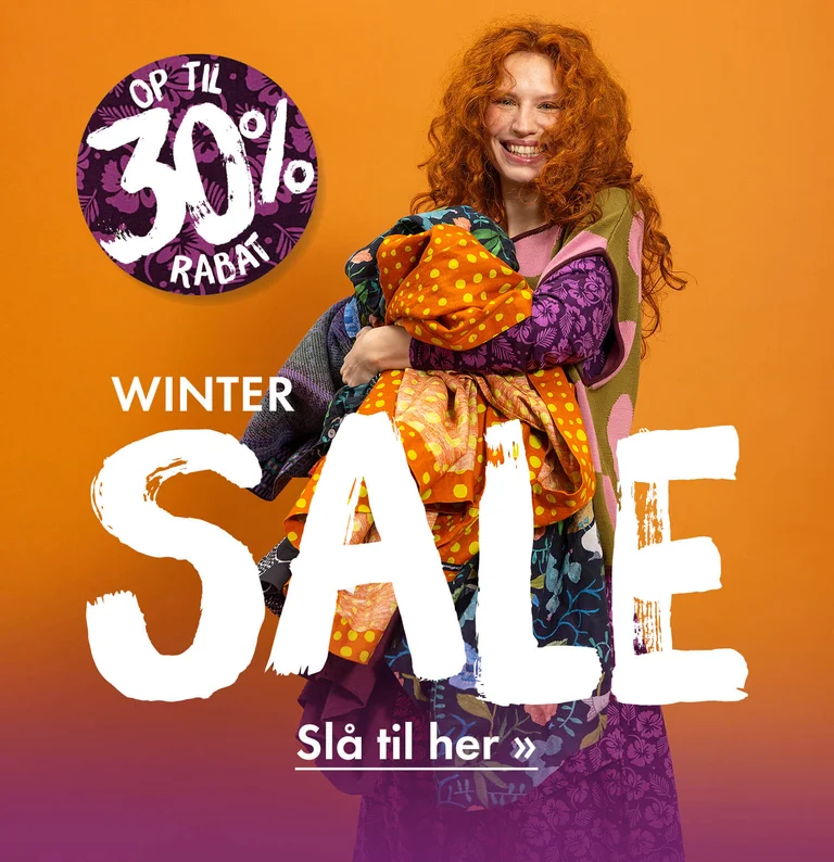 En kvinde med favnen fuld af farverigt tøj fra Gudrun Sjödén.