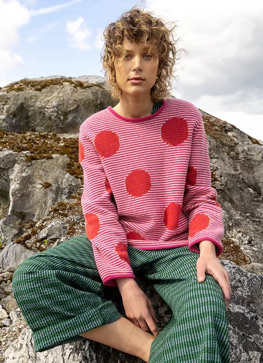 A woman wearing a rosy-red knit sweater and green pants from Gudrun Sjödén.