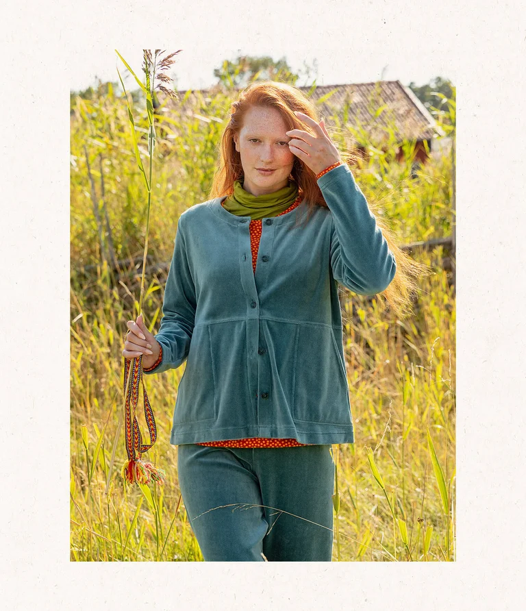 A woman outdoors wearing a turquoise velour cardigan with matching velour pants from Gudrun Sjödén.
