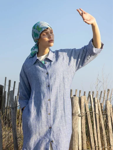 A woman wearing a light layered dress from Gudrun Sjödén, photographed from behind against a painted sea background.