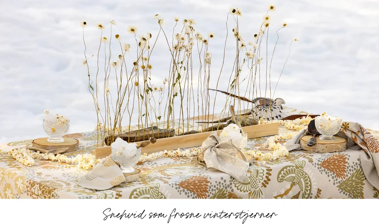 A table in the snow laid with home textiles from Gudrun Sjödén’s 2025 Christmas Home collection.