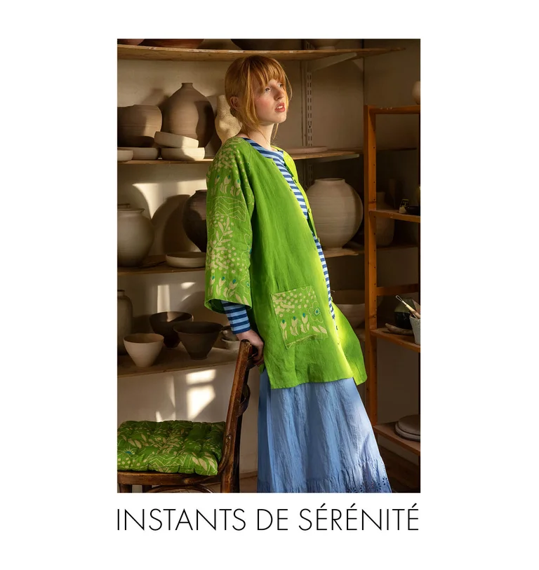 A woman in a pottery studio wearing a green “Nemorosa” linen tunic, a striped top and a light-blue skirt from Gudrun Sjödén.