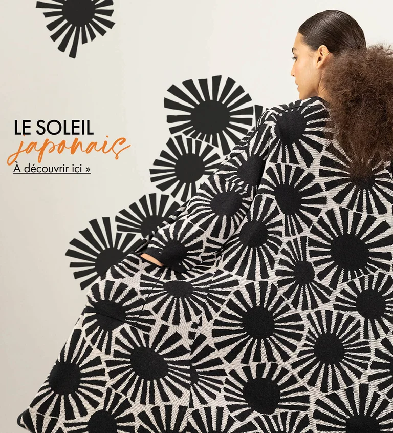 Une femme, dos à la caméra, portant un long gilet à motif paré de soleils graphiques noirs signé Gudrun Sjödén. Le motif se prolonge à l'extérieur de l'image, comme s'il s'évadait du gilet.