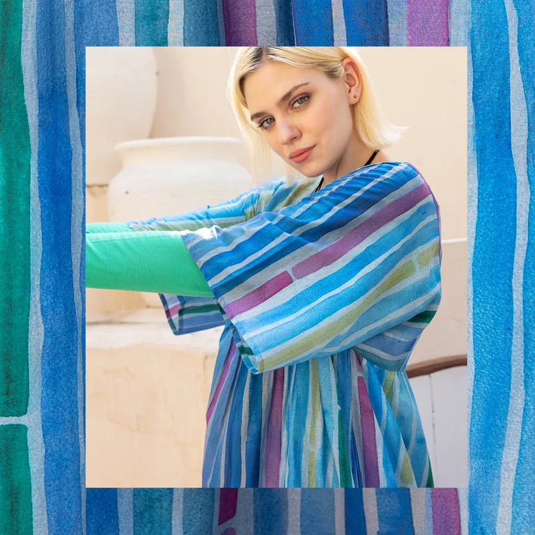 A woman wearing a blue, striped dress from Gudrun Sjödén’s Paris collection. There is a frame with the same pattern as on the dress around the picture.