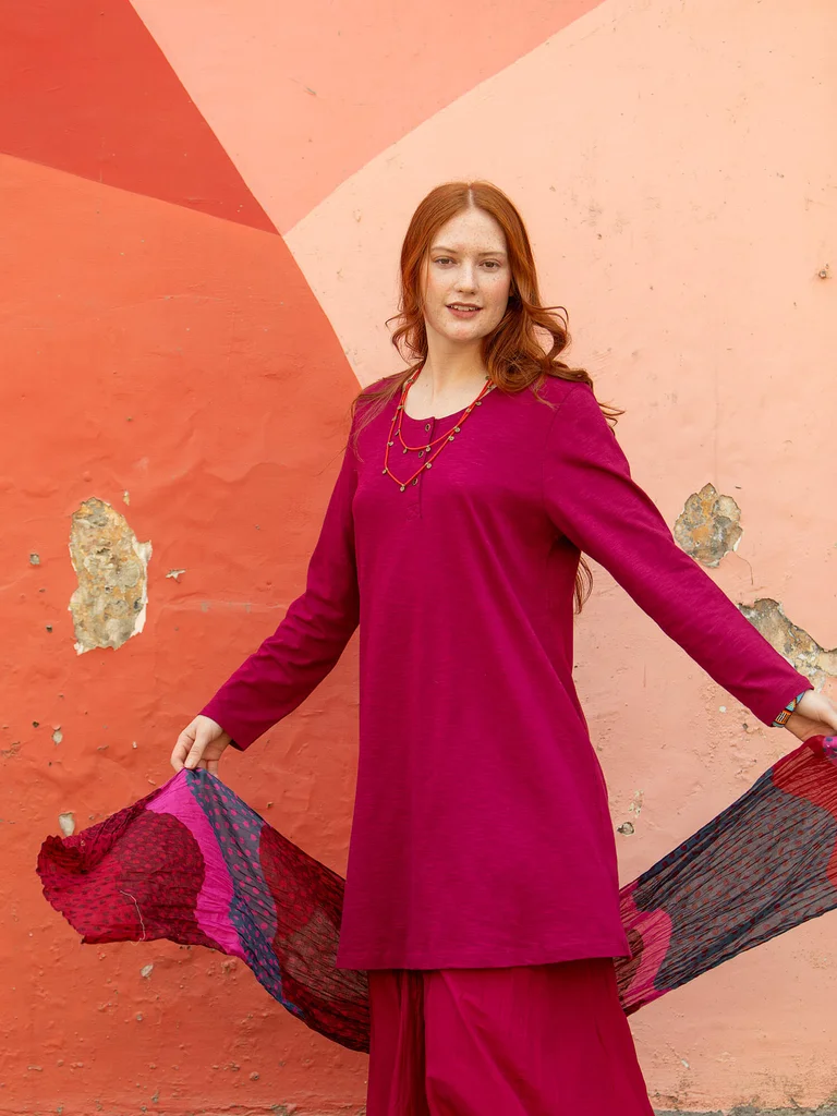 A woman wearing a red tunic and patterned shawl from Gudrun Sjödén. 