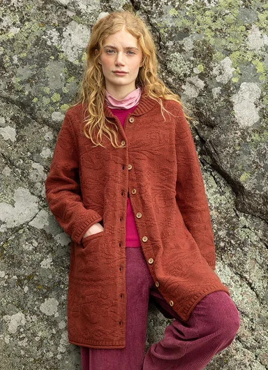 Eine Frau in einer Strickjacke in Braun-Orange von Gudrun Sjödén. 