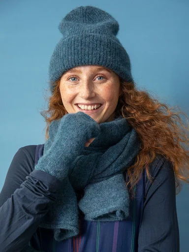 A woman wearing a blue beanie, scarf and fingerless gloves from Gudrun Sjödén. 