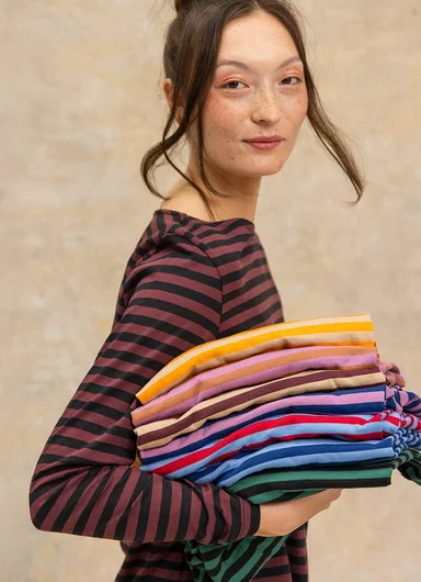 A woman wearing a striped sweater, holding a pile of striped sweaters from Gudrun Sjödén in her arms.