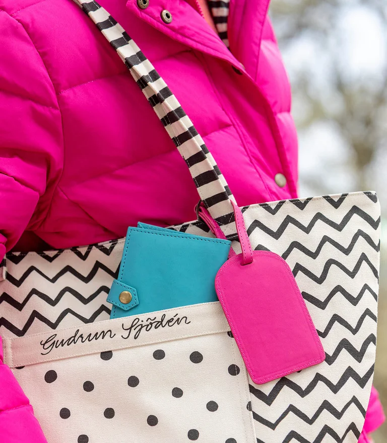 A closeup of a fabric tote bag, passport case and leather luggage tag from Gudrun Sjödén.