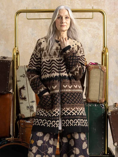 A woman standing in front of a luggage cart wearing layers of patterned brown clothing from Gudrun Sjödén.