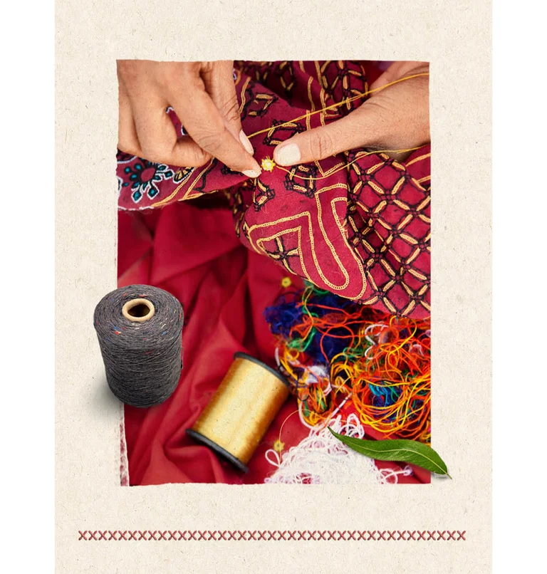 En närbild på händer som syr mönster med en guldtråd på ett rött tyg. I bilden finns även en frilagdtrådrulle och andra trådar i olika färger som ligger huller om buller. 