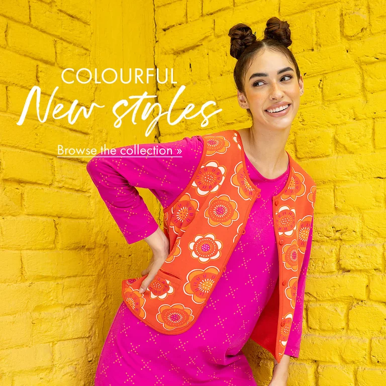 Two women posing against a yellow brick wall, wearing colourful clothes from Gudrun Sjödén.