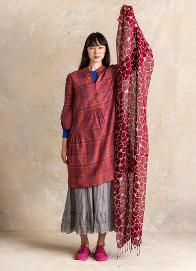 A woman holding up a burgundy patterned scarf from Gudrun Sjödén.